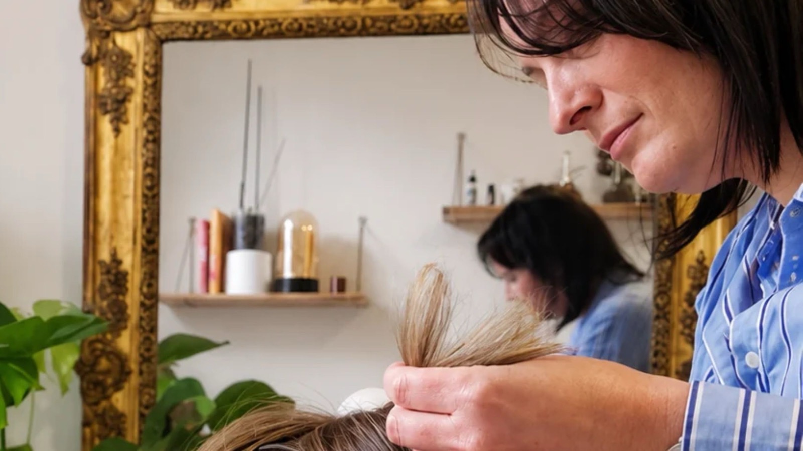 Au cabinet WavOïa, la trichothérapeute examine une mèche de cheveux, devant un miroir doré et des plantes
