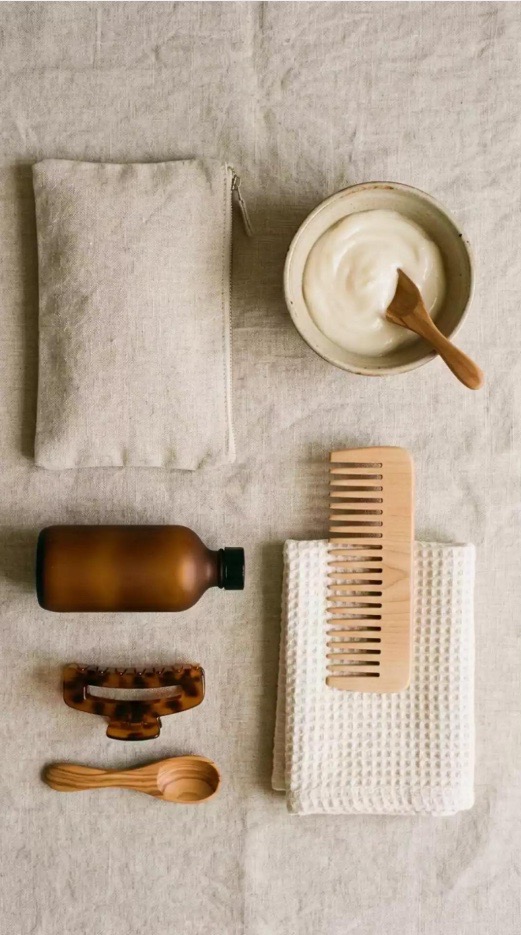 Bol de masque, peigne en bois, serviette gaufrée, flacon ambré, pince et cuillère en bois posés sur du lin